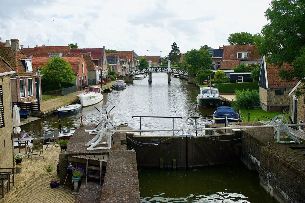 Sluis in Hindeloopen met houten sluisdeuren, boten langs de kade en een wit houten bruggetje over de vaart